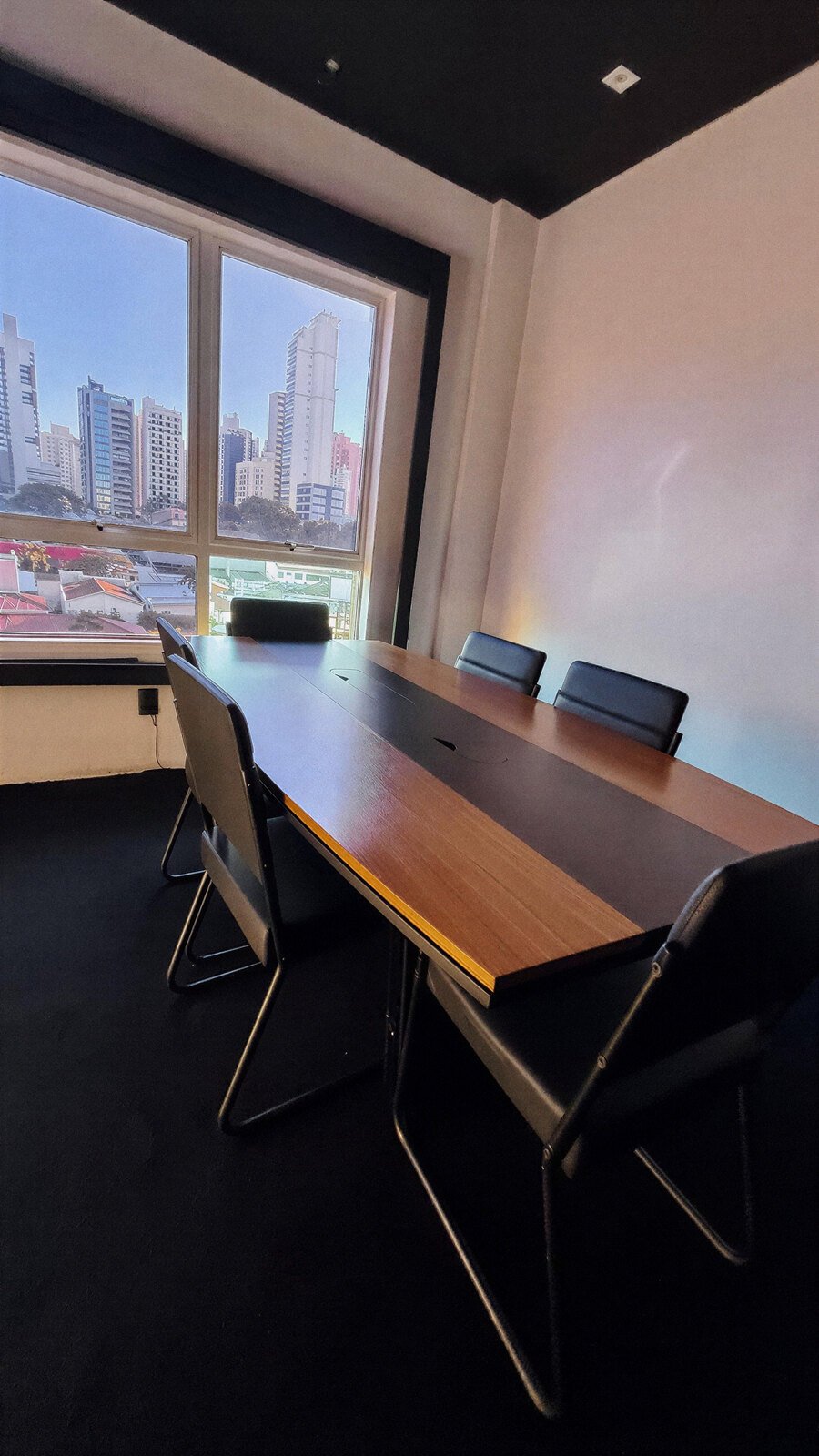 Sala de reuniões com mesa de madeira e vista para os prédios de Campinas