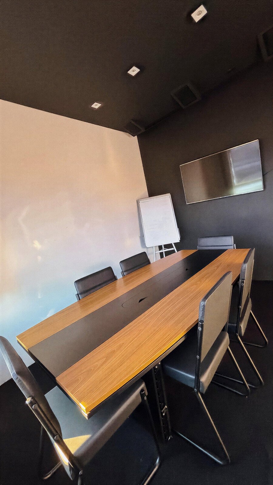 Sala de reuniões com mesa de madeira, cadeiras de couro e televisão