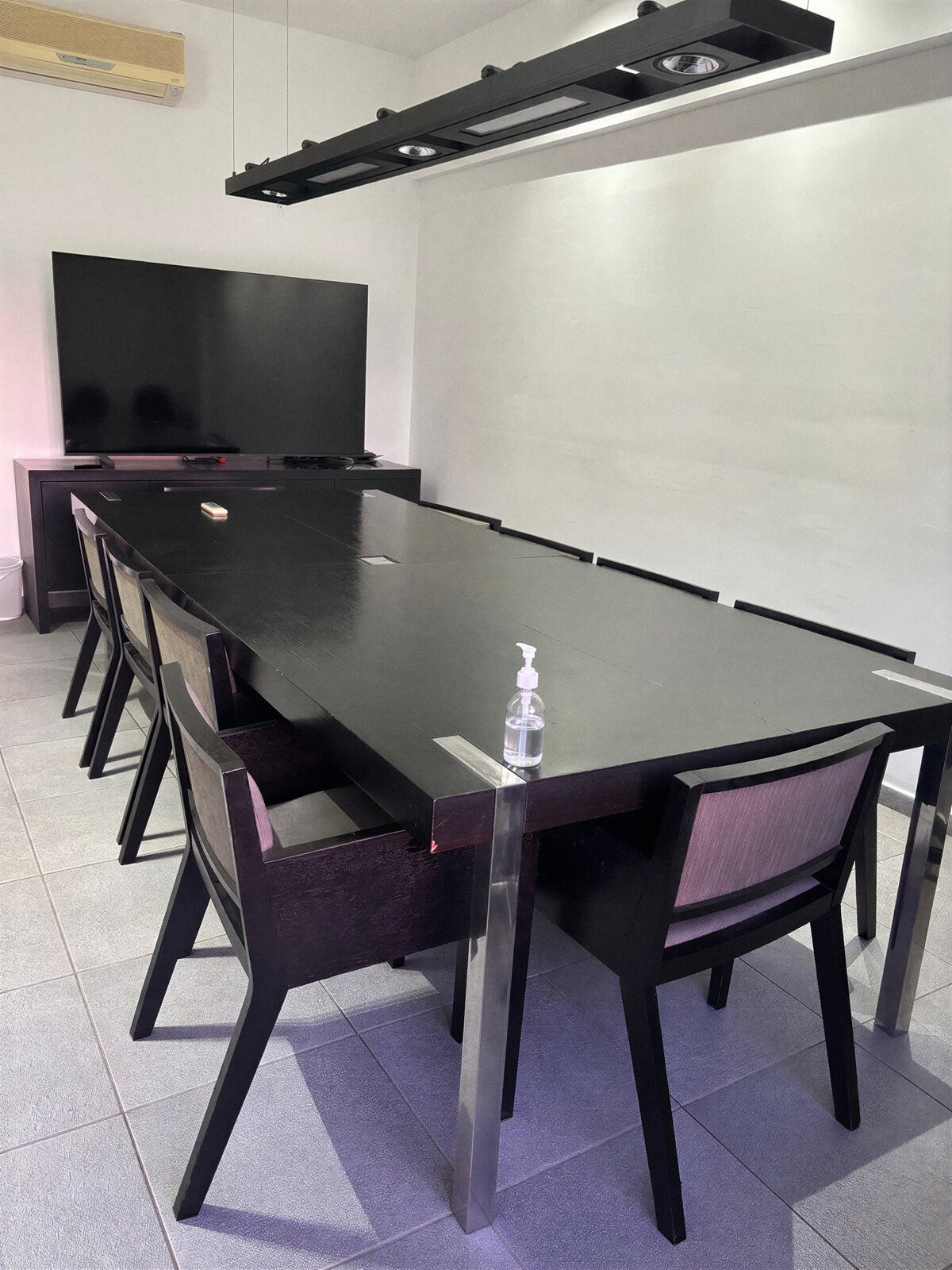 Sala de reuniões com mesa preta e televisão para atendimentos